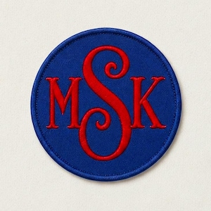 May include: A circular embroidered patch featuring a royal blue background with a red monogram in the centre. The monogram consists of the letters M, S, and K, with the central letter S being larger and more ornate than the letters M and K.