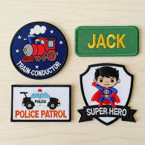 Könnte beinhalten: Vier gestickte Aufnäher: ein blauer Kreis mit einem roten Zug und "TRAIN CONDUCTOR", ein grünes Rechteck mit "JACK", ein weißes Rechteck mit einem Polizeiauto und "POLICE PATROL" und ein Schild mit einem Superhelden und "SUPER HERO".
