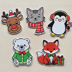 Puede incluir: Conjunto de cinco parches bordados con diseños de animales festivos. Incluye un reno con gorro de Papá Noel, un gato gris con bufanda roja, un pingüino con orejeras y bastón de caramelo, un oso polar con abrigo verde y un zorro con un regalo.