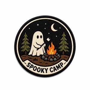 May include: A circular embroidered patch featuring a white ghost roasting a marshmallow over a campfire. The scene includes two green pine trees, a crescent moon, and stars against a black sky. The text SPOOKY CAMP is printed in black.