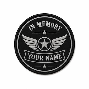 Könnte beinhalten: Ein runder, schwarz bestickter Aufnäher mit weißen Stickereien. Der Text IN MEMORY ist oben gebogen, mit YOUR NAME auf einem Banner unten. Ein zentraler Stern wird von zwei Flügeln flankiert, mit kleineren Sternen über und unter dem Motiv.