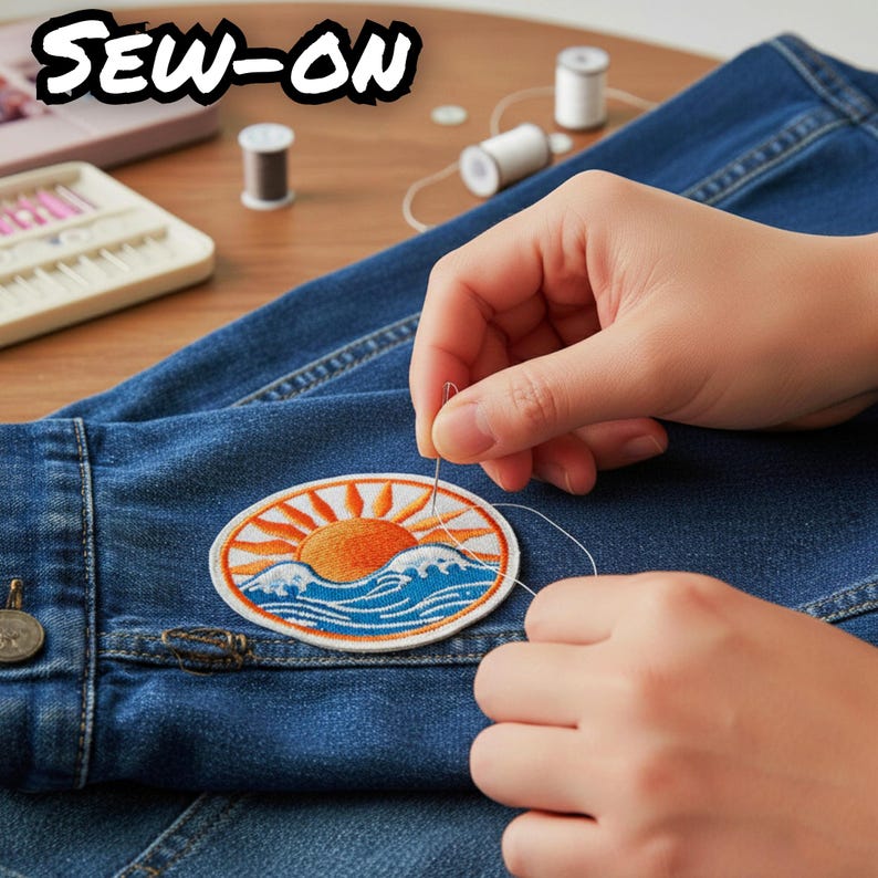 Pu&ograve; includere: Una toppa ricamata circolare raffigurante un sole che sorge sopra onde oceaniche blu, cucita su un tessuto denim blu scuro con ago e filo bianco. La toppa presenta un sole arancione, raggi bianchi e acqua blu con dettagli di schiuma.
