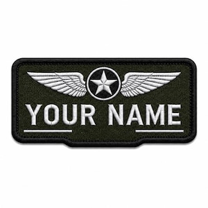 Könnte beinhalten: Ein rechteckiger, schwarz bestickter Aufnäher mit einem weißen geflügelten Stern-Emblem in der Mitte oben. Unter dem Emblem ist der Text YOUR NAME in weißen Großbuchstaben gestickt, unterstrichen von einer weißen Linie mit abgerundeten Kanten.
