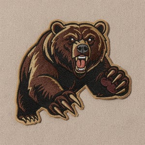 May include: An embroidered patch featuring a brown grizzly bear in a charging pose with its mouth open, showing teeth and a pink tongue. The bear has dark brown fur, tan highlights, and sharp claws, outlined with a tan border on a textured background.