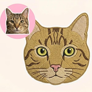 以下が含まれることがあります： ベージュ、茶色、黄色の刺繍入り猫の顔パッチ。パッチは、緑の目とピンクの鼻を持つ詳細な猫の顔を示しています。猫の顔の小さな画像が、左上隅のピンク色の円の中にあります。