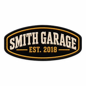 Op de afbeelding: Een ovaalvormige geborduurde patch met een zwarte achtergrond en een gouden rand. De tekst SMITH GARAGE is in het wit geborduurd in een boog aan de bovenkant. Daaronder staat de tekst EST. 2018 in goud, geflankeerd door twee gouden lijnen.