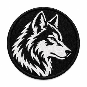 Op de afbeelding: Een ronde geborduurde patch met een contrastrijk zwart-wit ontwerp van een wolvenkop in profiel. De wolf is afgebeeld met scherpe, gestileerde vachtdetails en een gefocuste uitdrukking, ingesloten binnen een dikke, zwart gestikte rand.