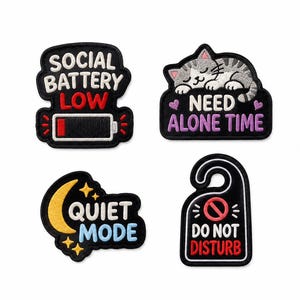 Puede incluir: Cuatro parches bordados con fondo negro. Uno dice SOCIAL BATTERY LOW con un icono de batería. Otro muestra un gato y dice NEED ALONE TIME. Uno presenta una luna creciente amarilla y dice QUIET MODE. Uno tiene forma de colgador de puerta y dice DO NOT DISTURB.