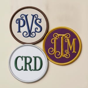 Puede incluir: Tres parches bordados circulares con letras de monograma. Un parche es crema con letras PVS azul oscuro y borde marrón. Otro es morado con letras JJM doradas y borde dorado. El tercero es blanco con letras CRD verdes y borde plateado.