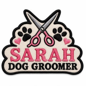 Peut inclure: Un écusson brodé sur fond crème avec une bordure noire. Il présente une paire de ciseaux de toilettage argentés et roses, deux empreintes de pattes noires et deux petits cœurs roses. Le texte SARAH est en rose et DOG GROOMER en noir.