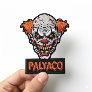 May include: Embroidered patch depicting a scary clown face with orange hair, a red nose, and stitched orange cross-shaped eyes. The clown has a wide, menacing grin with sharp teeth. Below the clown is a black rectangle with the word "PALYACO" in orange.