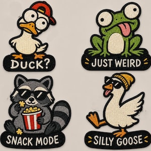 Könnte beinhalten: Vier bestickte Aufnäher mit Zeichentricktieren: eine Ente mit roter Kappe und der Aufschrift DUCK?, ein grüner Frosch mit JUST WEIRD, ein Waschbär mit Popcorn und SNACK MODE sowie eine Gans mit gelber Mütze und Sonnenbrille mit SILLY GOOSE.