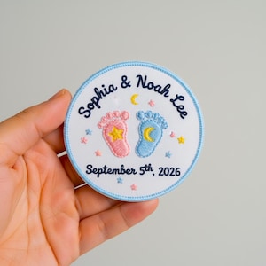 May include: Embroidered patch with a light blue border, featuring the names "Sophia & Noah Lee" and the date "September 5th, 2026." The design includes pink and blue baby footprints, a star, and a crescent moon.
