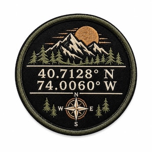 May include: A circular embroidered patch with a black background featuring a mountain range, a golden sun, and green pine trees. The text 40.7128° N 74.0060° W is centered above a compass rose with cardinal directions N, S, E, and W in white thread.