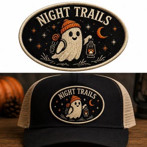 Könnte beinhalten: Eine schwarze Trucker-Cap mit einem ovalen, bestickten Aufnäher mit dem Text NIGHT TRAILS. Der Aufnäher zeigt einen weißen Geist mit orangefarbener Mütze, Rucksack und Laterne, umgeben von Sternen und einer Mondsichel auf schwarzem Grund.