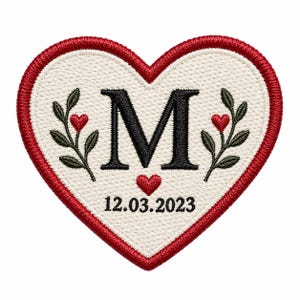 May include: A heart-shaped embroidered patch with a cream-coloured background and a thick red border. The centre features a large black letter M, flanked by two green leafy branches with small red hearts, and the date 12.03.2023 printed below.