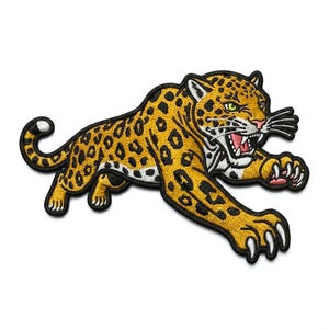 May include: Embroidered patch featuring a leaping jaguar with a yellow and black spotted coat. The jaguar has a white face, pink mouth, and sharp teeth. The patch is outlined in black.