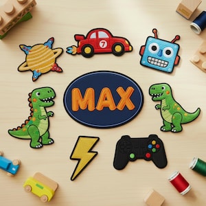 May include: A collection of embroidered patches featuring a red car, a blue robot, two green dinosaurs, a yellow lightning bolt, a black game controller, and a blue oval patch with the name "MAX" in orange letters. The patches are on a light wood surface.