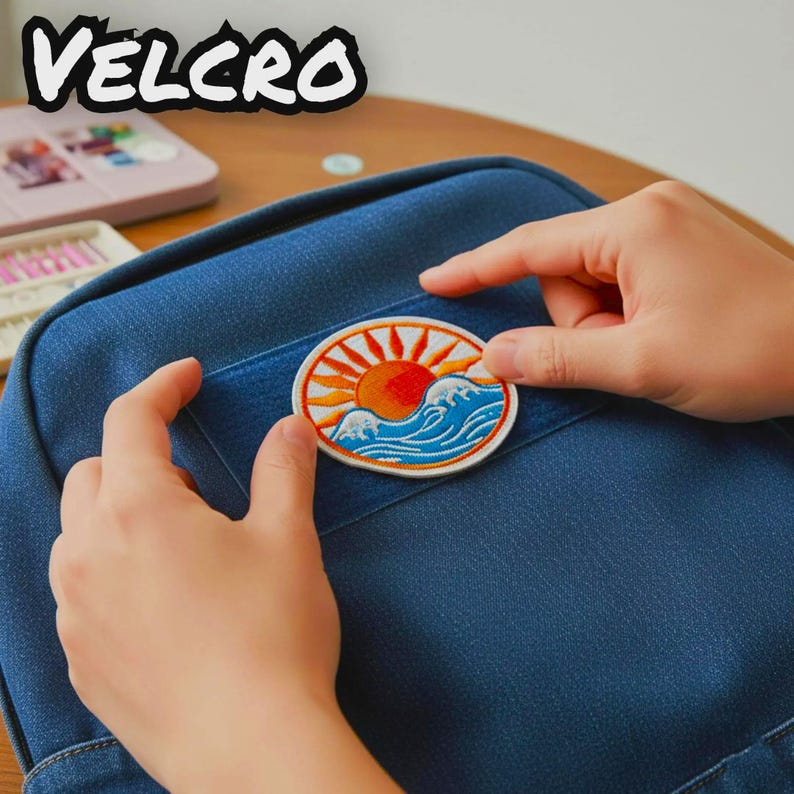 K&ouml;nnte beinhalten: Ein runder, bestickter Aufn&auml;her mit einer Sonne, die &uuml;ber blauen Meereswellen aufgeht, befestigt an einer dunkelblauen Jeanstasche. Der Aufn&auml;her hat einen wei&szlig;en Rand und leuchtend orangefarbene und gelbe Sonnenstrahlen. Das Wort VELCRO steht oben links.