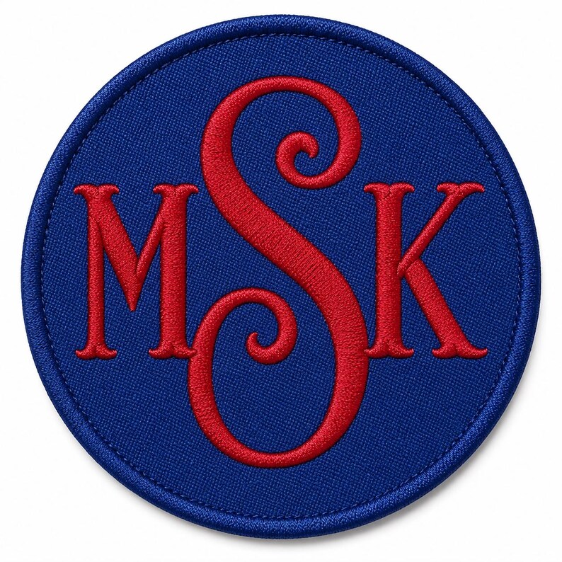 May include: A circular embroidered patch featuring a deep blue background with a stitched border. The centre displays the letters M, S, and K in a bold red thread. The letter S is larger and positioned centrally between the M and K characters.