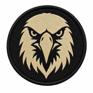May include: A circular embroidered patch featuring a stylised eagle head design. The eagle is rendered in light tan thread against a solid black background, with a thick black stitched border framing the circular shape of the patch.