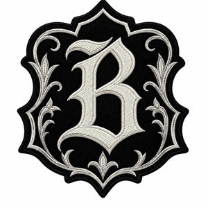 May include: A black embroidered patch in a shield shape featuring a large white letter B in a gothic font style. The letter is surrounded by intricate white stitched floral scrollwork and filigree patterns that follow the curved edges.
