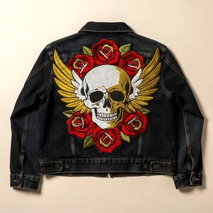 May include: Dark denim jacket with a large embroidered design on the back. The design features a skull with gold wings, surrounded by red roses. The jacket has a classic collar, button closures, and pockets.