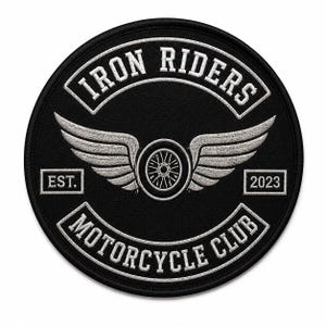 May include: A circular black embroidered patch featuring white stitching. The text reads IRON RIDERS at the top and MOTORCYCLE CLUB at the bottom. A central graphic shows a motorcycle wheel with wings, flanked by the text EST. and 2023 on the sides.