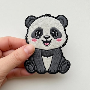 Puede incluir: Parche bordado de un oso panda sonriente. El panda tiene un cuerpo negro y blanco, mejillas rosadas y un contorno negro. El parche está diseñado para ser cosido o planchado sobre tela.