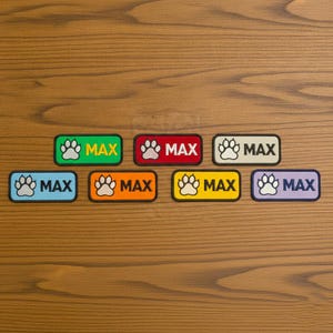 Puede incluir: Siete parches rectangulares bordados que presentan un icono de huella a la izquierda y el nombre MAX en letras mayúsculas a la derecha. Los parches vienen en verde, rojo, crema, azul claro, naranja, amarillo y morado con bordes oscuros.