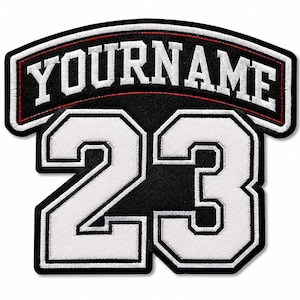Könnte beinhalten: Ein schwarz-weiß bestickter Aufnäher mit dem Text YOURNAME in fetter Schrift auf einem gewölbten Banner über der großen Zahl 23. Das Design hat einen schwarzen Hintergrund mit weißer Schrift und Ziffern, umrandet von weißen und dünnen roten Nähten.