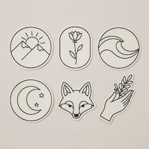 May include: A collection of six white stickers with black line art designs. The designs include a mountain scene with a sun, a flower, ocean waves, a crescent moon with stars, a fox head, and a hand holding a sprig.