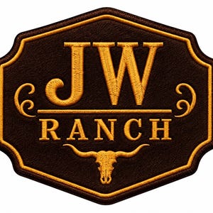 Puede incluir: Un parche de color marrón oscuro en forma de escudo con el texto JW RANCH bordado en hilo dorado. El diseño incluye una línea horizontal, remolinos decorativos a los lados y un icono de cráneo de toro centrado en la parte inferior, bordeado en oro.