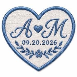 Puede incluir: Un parche bordado en forma de corazón con fondo blanco y borde azul. El diseño presenta las letras A y M separadas por un pequeño corazón, la fecha 09.20.2026 y un motivo de rama floral en la parte inferior, todo bordado con hilo azul.