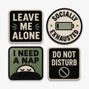 Op de afbeelding: Vier geborduurde patches met crèmekleurige randen. Linksboven: zwart vierkant met witte tekst LEAVE ME ALONE. Rechtsboven: ronde crèmekleurige patch met zwarte tekst SOCIALLY EXHAUSTED en batterijpictogram. Linksonder: groen vierkant met I NEED A NAP en een slapende figuur. Rechtsonder: zwart vierkant met DO NOT DISTURB en een verbodsteken.