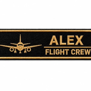 May include: A rectangular black embroidered patch with a gold border. On the left, a gold aeroplane icon is depicted. On the right, the text ALEX is printed above a horizontal line, with the words FLIGHT CREW printed below the line in gold.