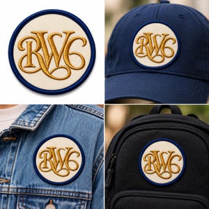 May include: A circular embroidered patch featuring the gold-stitched letters RWC on a cream-coloured background with a dark blue border. The patch is shown applied to a navy blue baseball cap, a blue denim jacket, and a black fabric backpack.