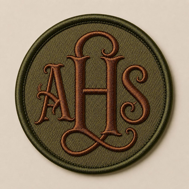May include: A circular embroidered patch featuring an olive green background with a dark brown stitched border. The center displays the letters AHS in a decorative, interlocking serif font, also stitched in a dark brown thread color.