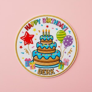 May include: Embroidered patch with a birthday cake design. The patch features a three-tiered cake with blue frosting, lit candles, and the words "HAPPY BIRTHDAY!" and "BERK". Colorful balloons, stars, and gift boxes complete the festive design.