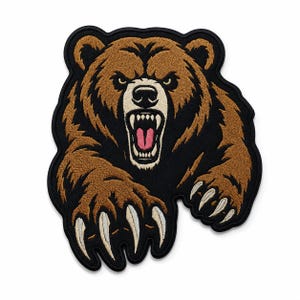 Puede incluir: Un parche bordado que muestra un oso pardo sobre un fondo negro. El oso aparece con la boca abierta, dientes visibles, una lengua rosa y garras blancas afiladas extendidas hacia adelante. El diseño tiene un borde negro grueso.