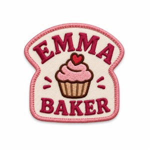 Könnte beinhalten: Ein brotförmiger Aufnäher mit cremefarbenem Hintergrund und rosa Rand. Der Text EMMA BAKER ist in Dunkelrosa gestickt. In der Mitte befindet sich ein Cupcake mit rosa Zuckerguss und einem kleinen roten Herz über dem Wort BAKER.
