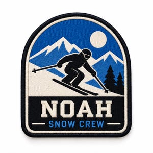 May include: An embroidered patch with a black border featuring a skier in black silhouette against blue mountains, a white sun, and pine trees. The lower section is black with the white text NOAH and the blue text SNOW CREW below it.