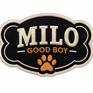 May include: A bone-shaped embroidered patch with a black background and a cream-coloured border. The text MILO is stitched in large cream letters above the words GOOD BOY in smaller gold letters, with a gold paw print icon centred at the bottom.