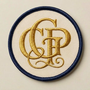 May include: A circular embroidered patch featuring a cream-colored fabric base with a dark navy blue stitched border. Centered on the patch is an ornate, metallic gold thread monogram consisting of the intertwined capital letters C and P.