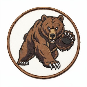 May include: A circular embroidered patch featuring a brown grizzly bear with a tan muzzle and white claws. The bear is depicted in a forward-facing, aggressive stance with one paw raised. The design is set against a white background with a brown border.