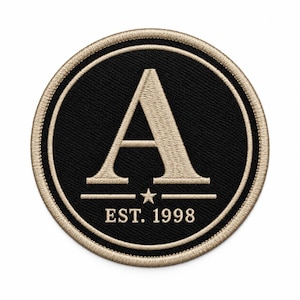 Peut inclure: Un écusson brodé circulaire avec un fond noir et une bordure dorée. Le centre présente une grande lettre A dorée au-dessus d'une petite étoile dorée et du texte EST. 1998 en doré. Le motif est fini avec un bord cousu doré épais.