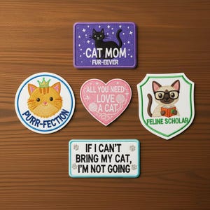 Puede incluir: Un conjunto de parches bordados con diseños temáticos de gatos. Los parches incluyen un rectángulo morado con un gato negro y el texto "CAT MOM FUR-EEVER", un parche redondo con un gato y el texto "PURR-FECTION", un parche en forma de corazón con el texto "ALL YOU NEED LOVE A CAT", un parche en forma de escudo con un gato con gafas y el texto "FELINE SCHOLAR", y un parche rectangular con el texto "IF I CAN'T BRING MY CAT, I'M NOT GOING".
