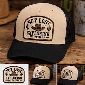Może przedstawiać: Beżowo-czarna czapka typu trucker z prostokątną naszywką o zaokrąglonych rogach. Naszywka zawiera napis NOT LOST EXPLORING MY OPTIONS, ilustrację brązowego kapelusza kowbojskiego oraz dwie zielone ikony kaktusów na jasnym tle.
