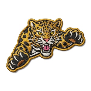 May include: Embroidered patch featuring a leaping jaguar with a fierce expression. The patch has a yellow and black spotted design, with a gold border. The jaguar's mouth is open, revealing its pink tongue and white teeth. Its claws are extended.