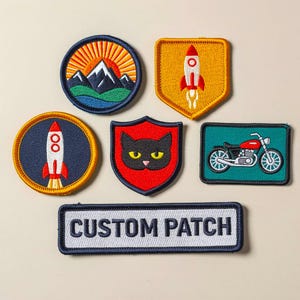 May include: A collection of embroidered patches featuring various designs. Included are a mountain scene, a rocket, a black cat, a motorcycle, and a patch that says "CUSTOM PATCH". The patches are in various shapes and colors.
